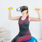 young-woman-wearing-virtual-reality-headset-sitting-fitness-ball-exercising-with-yellow-dumbbells